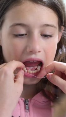 Bir anne küçük kızına diş ipi kullanarak bebek dişini çekiyor. Dikey video