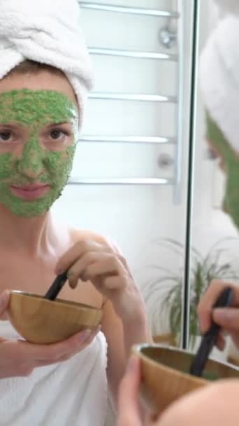 白いタオルが彼女の顔に置かれた若い女性 カメラで笑顔と面白い顔を作る緑の保湿マスク — ストック動画