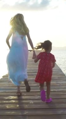 Doğan güneşe doğru bir ahşap deniz iskele üzerinde çalışan küçük kızı olan kadın