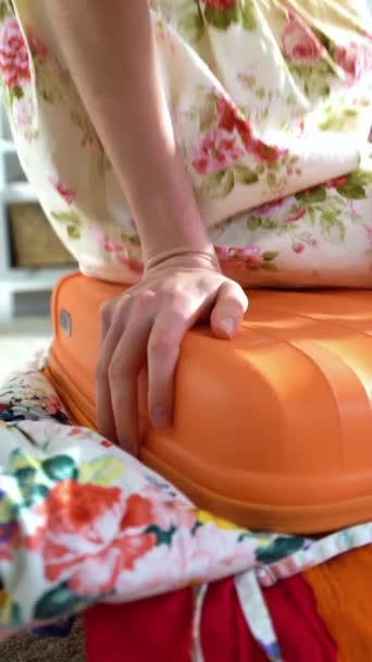 若い女性がぎっしりのオレンジ色のスーツケースを閉じるしよう — ストック動画