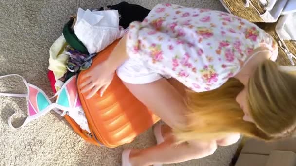 Молодая Женщина Пытается Закрыть Полный Оранжевый Чемодан Вид Сверху — стоковое видео