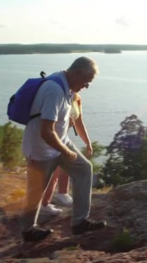 Kaya tırmanışı ve güneşin doğuşunu hayran yaşlı aktif çift gün batımı. Deniz ve çam ağaçları, İskandinavya yatay.