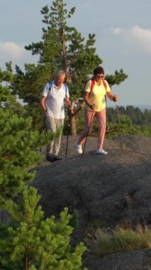 Kaya tırmanışı ve güneşin doğuşunu hayran yaşlı aktif çift gün batımı. Deniz ve çam ağaçları, İskandinavya yatay.