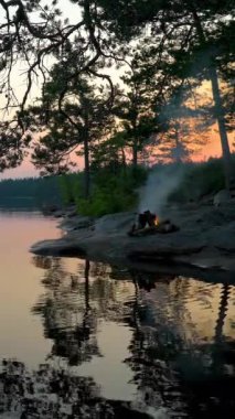 Yaz Gündönümünde gece yarısı gölün kıyısındaki bir ormanda yanan şenlik ateşi. Finlandiya 'da yaz dönümü arifesinde Beyaz Gece. Kamp ateşi ve vahşi yaşam sesleri, kuş sesleri.