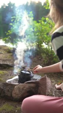 Orman gölünün kıyısındaki çadırda gün batımında sessizlik, doğa, özgürlük ve yalnızlığın tadını çıkaran genç bir kadın. Dikey odaklı bir video.