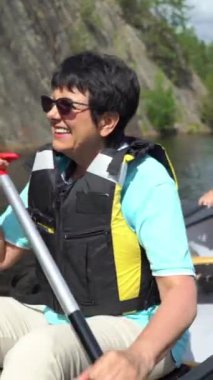 Yaşlı çift Finlandiya 'da bir orman gölünde kano yapıyor. Aktif emekliler açık hava sporlarını severler. Sportif yaşlı insanlar doğayla eğleniyorlar. Dikey odaklı bir video.