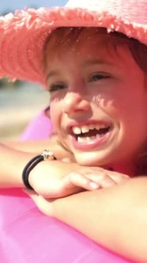 Güneşli bir sahilde şişme pembe bir kanepede pembe hasır şapka takan mutlu küçük bir kız. Coronavirus salgından sonraki yaşam..