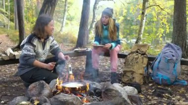 Finlandiya 'da yürüyüş yaparken, kamp alanında açık ateş üzerinde geleneksel krep pişiren bayan arkadaşlar, sessizliğin ve temiz havanın tadını çıkarıyorlar.
