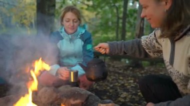 İki bayan arkadaş, Finlandiya 'da yürüyüş yaparken sessizliğin ve temiz havanın tadını çıkararak ormanda açık ateşte kahve yapıyorlar.