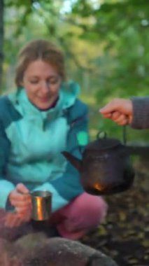 İki bayan arkadaş, Finlandiya 'da yürüyüş yaparken sessizliğin ve temiz havanın tadını çıkararak ormanda açık ateşte kahve yapıyorlar. Dikey odaklı bir video.