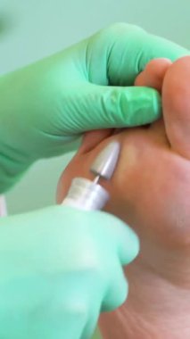 Pedikür uzmanı güzellik salonunda estetik donanım pedikürü yapıyor. Tıp ve estetik bir ofiste genç bir kadının parmaklarını, tırnaklarını ve ayaklarını tedavi eden bir pedikür uzmanı.
