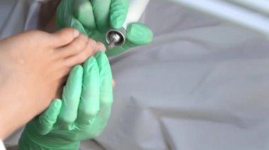 Pedikür uzmanı güzellik salonunda estetik donanım pedikürü yapıyor. Tıp ve estetik bir ofiste genç bir kadının parmaklarını, tırnaklarını ve ayaklarını tedavi eden bir pedikür uzmanı.