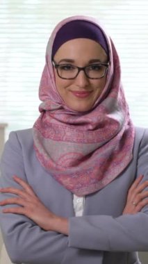 Geleneksel başörtüsü takmış, kameraya bakıp gülen genç Müslüman kadın portresi. Akıllı telefon ekranı, hedef sosyal medya platformları ve web tarayıcıları için dikey video