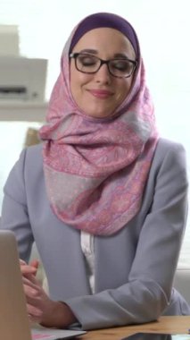 Geleneksel başörtüsü takmış, kameraya bakıp gülen genç Müslüman kadın portresi. Akıllı telefon ekranı, hedef sosyal medya platformları ve web tarayıcıları için dikey video