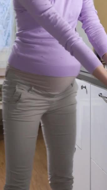 妊娠中の若い女性は明るい晴れたキッチンでディッシュウォッシャーマシンからきれいな皿を取り出します 持続可能なライフスタイルのための信頼性と安全な家庭用品 バーティカルビデオ — ストック動画