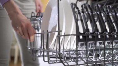 Parlak güneşli bir mutfakta Bulaşık Makinesinden Temiz Bulaşık Çıkaran Genç Kadın. Sürdürülebilir Yaşam Tarzları İçin Güvenilir ve Güvenli Ev Aletleri. Ev hanımı modern aletleri kullanıyor.