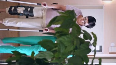 Bayan bakıcı, kadın hastasına bacak yaralanmasında yardım ediyor, elini tutuyor, onu destekliyor. Üniformalı tesettürlü genç Müslüman hemşire, yanında yürürken olgun yaşlı bir kadına destek oluyor.