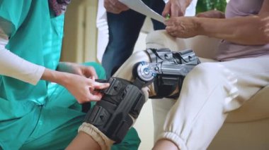 Başörtüsü takan genç Müslüman hemşire, klinikteki ya da hastanedeki uzman doktorla iletişim kuran yaşlı bir kadın hastanın bacağına kölelik, dizlik ve tıbbi destek takmaya yardım ediyor.