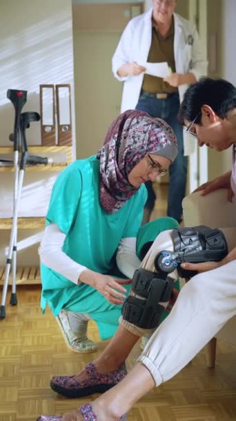 Young Muslim Nurse Wearing Hijab Helps Put Bondage Knee Brace — Stock Video