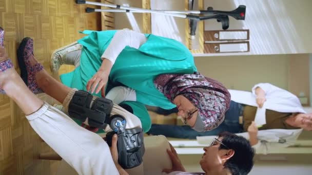 年轻的穆斯林护士头戴头巾 帮助在与诊所或医院的主治医生交流的老年女性病人的腿上绑上镣铐 医疗夹板 — 图库视频影像