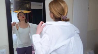 Genç yetişkin bir kadın yatak odasında aynanın önünde giyiniyor. Sabah uyanma konsepti.