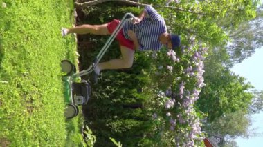 Orta yaşlı bir adam bahçesinde çim biçme makinesiyle fazla büyümüş yeşil çimenleri buduyor. Şortlu erkek bahçıvan bahçe düzenlerken çim biçme makinesi kullanıyor. Mevsimlik iş kavramı.