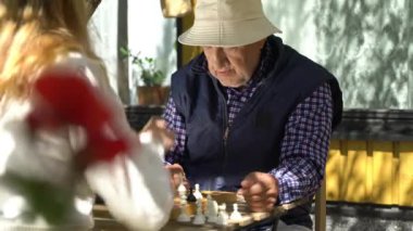 Yaşlı adam ve genç kadın bahçede satranç oynuyorlar. Boş zaman aktivitesi, akıl sağlığı ve yaşlılık, spor, eğlence, eski nesil, mutlu emekli insanlar, sağlık ve