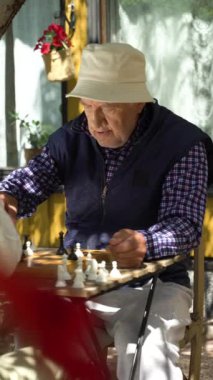 Yaşlı adam ve genç kadın bahçede satranç oynuyorlar. Boş zaman aktivitesi, akıl sağlığı ve yaşlılık, spor, eğlence, eski nesil, mutlu emekli insanlar, sağlık ve