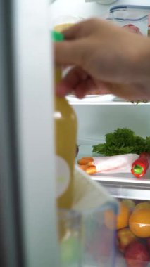 Dikey yönelimli video. Yiyecek dolu buzdolabının kapısını açan genç bir kadın.