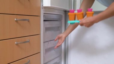 Ev yapımı buzlu şeker, dondurmalı lolipop, dondurulmuş meyve suyu. Genç bir kadın dondurmayı dondurucuya koyuyor.
