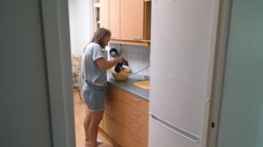 Evinin mutfağında yemek pişiren genç bir kadın. Karıştırıcı ile tatlı için pişirme ayinini çırp.