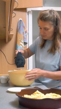 Evinin mutfağında yemek pişiren genç bir kadın. Karıştırıcı ile tatlı için pişirme ayinini çırp.