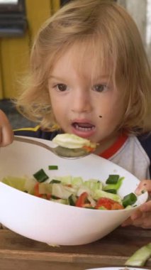 Küçük çocuk açık havada oturmuş taze sebze salatası yiyor. Çocuk sağlıklı besin konsepti