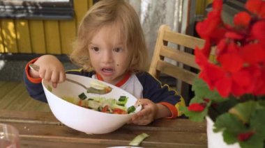 Küçük çocuk açık havada oturmuş taze sebze salatası yiyor. Çocuk sağlıklı besin konsepti