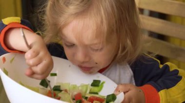 Küçük çocuk açık havada oturmuş taze sebze salatası yiyor. Çocuk sağlıklı besin konsepti