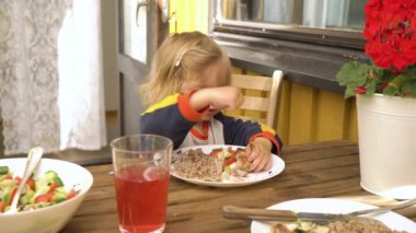 Küçük çocuk taze sebzeli tavuk yiyor. İştahlı. Çatalla dışarıda oturuyor. Çocuk sağlıklı besin konsepti