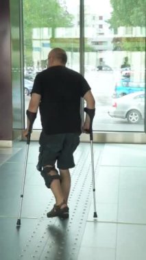Kölelik ve tıbbi desteğe sahip olgun bir adam. Bacağında dizlik var. Yürüyen merdivenden metroya koltuk değnekleriyle iniyor. Engelliler için erişilebilir kentsel ortam, yaralanma sonrası iyileşme.
