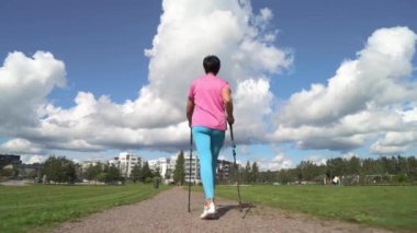 Spor giyimli atletik olgun bir kadın Finlandiya 'da bir şehir parkında İskandinav yürüyüşü yapıyor.