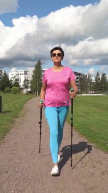 Spor giyimli atletik olgun bir kadın Finlandiya 'da bir şehir parkında İskandinav yürüyüşü yapıyor.