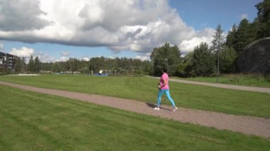 Spor giyimli atletik olgun bir kadın Finlandiya 'da bir şehir parkında İskandinav yürüyüşü yapıyor.