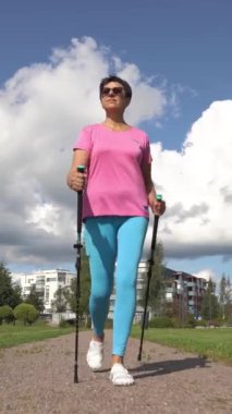 Spor giyimli atletik olgun bir kadın Finlandiya 'da bir şehir parkında İskandinav yürüyüşü yapıyor.