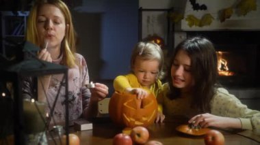 Anne, bebek ve kızı Cadılar Bayramı 'nda evde balkabağı kabağı yapıyorlar. Evde eğlenceli zanaat ve dekorasyon. Mutlu çocuklar ve anneleri tatil için hazırlanıyor.