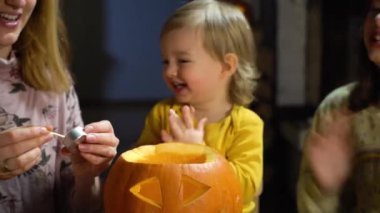Anne, bebek ve kızı Cadılar Bayramı 'nda evde balkabağı kabağı yapıyorlar. Evde eğlenceli zanaat ve dekorasyon. Mutlu çocuklar ve anneleri tatil için hazırlanıyor.