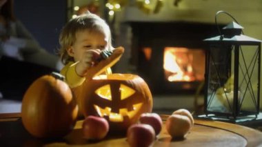 Cadılar Bayramı arifesinde oturma odasında yanan şömine arkaplanı olan eski ahşap masada balkabağı Jack-O-Lantern eğlenen küçük çocuk..