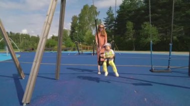 Bir anne ve küçük oğlu oyun alanında eğleniyor. Şehir parkında yürümeye başlayan çocuğuyla oynayan güzel bir kadın. Çocuklu aileler için geleneksel aktif mevsimlik eğlence
