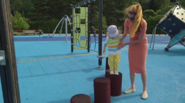 Bir anne ve küçük oğlu oyun alanında eğleniyor. Şehir parkında yürümeye başlayan çocuğuyla oynayan güzel bir kadın. Çocuklu aileler için geleneksel aktif mevsimlik eğlence