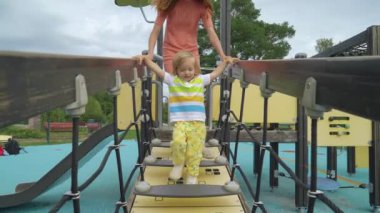 Bir anne ve küçük oğlu oyun alanında eğleniyor. Şehir parkında yürümeye başlayan çocuğuyla oynayan güzel bir kadın. Çocuklu aileler için geleneksel aktif mevsimlik eğlence