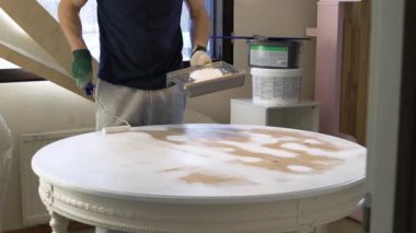 Orta yaşlı bir adam eski ahşap masayı beyaz renkli boyuyor. Mobilya onarımı, DIY onarımı, kendi kendine tamir edilmesi ve ev dekorasyonu.
