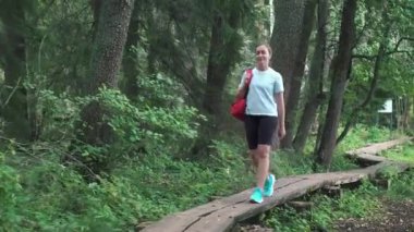 Sırt çantalı genç bir bayan gezgin Finlandiya 'daki ulusal parkta ahşap bir çevre yolunda yürüyor. Doğa yürüyüşü, dinlenme ve spor. Güzel kuzey ormanlarında macera