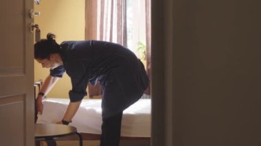 Otel odasında yatak değiştiren bir kadın hizmetçi. Kar beyazı çarşafları düzleştiren hizmetçi. Bir çalışan pansiyonda bir odayı temizliyor. Otel sektöründe kaliteli hizmet kavramı